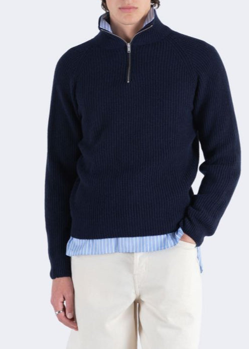 Man wearing a navy half-zip sweater over a light blue shirt with a white background