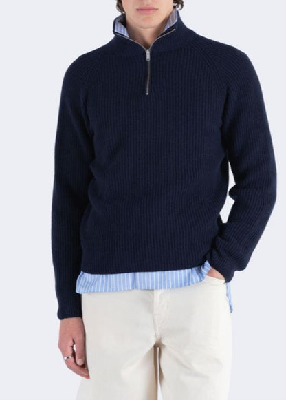 Man wearing a navy half-zip sweater over a light blue shirt with a white background